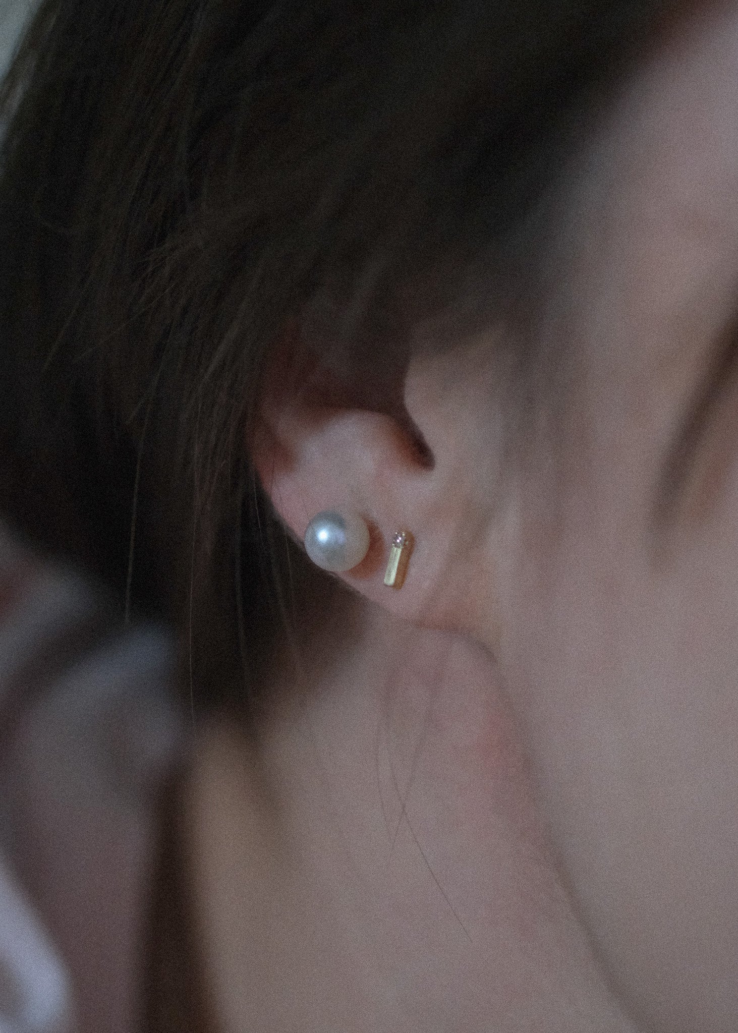 Close-up of a person's ear wearing a small white pearl stud earring and a tiny gold post earring.