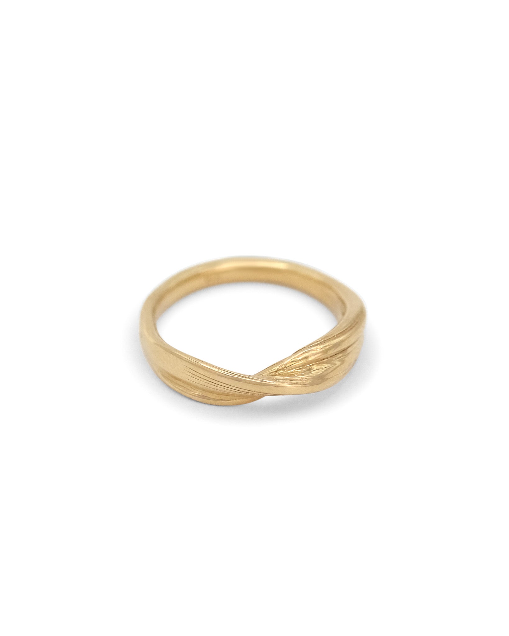 An 18 karat yellow gold wedding band with a twisted, overlapping band design, photographed against a seamless white background.