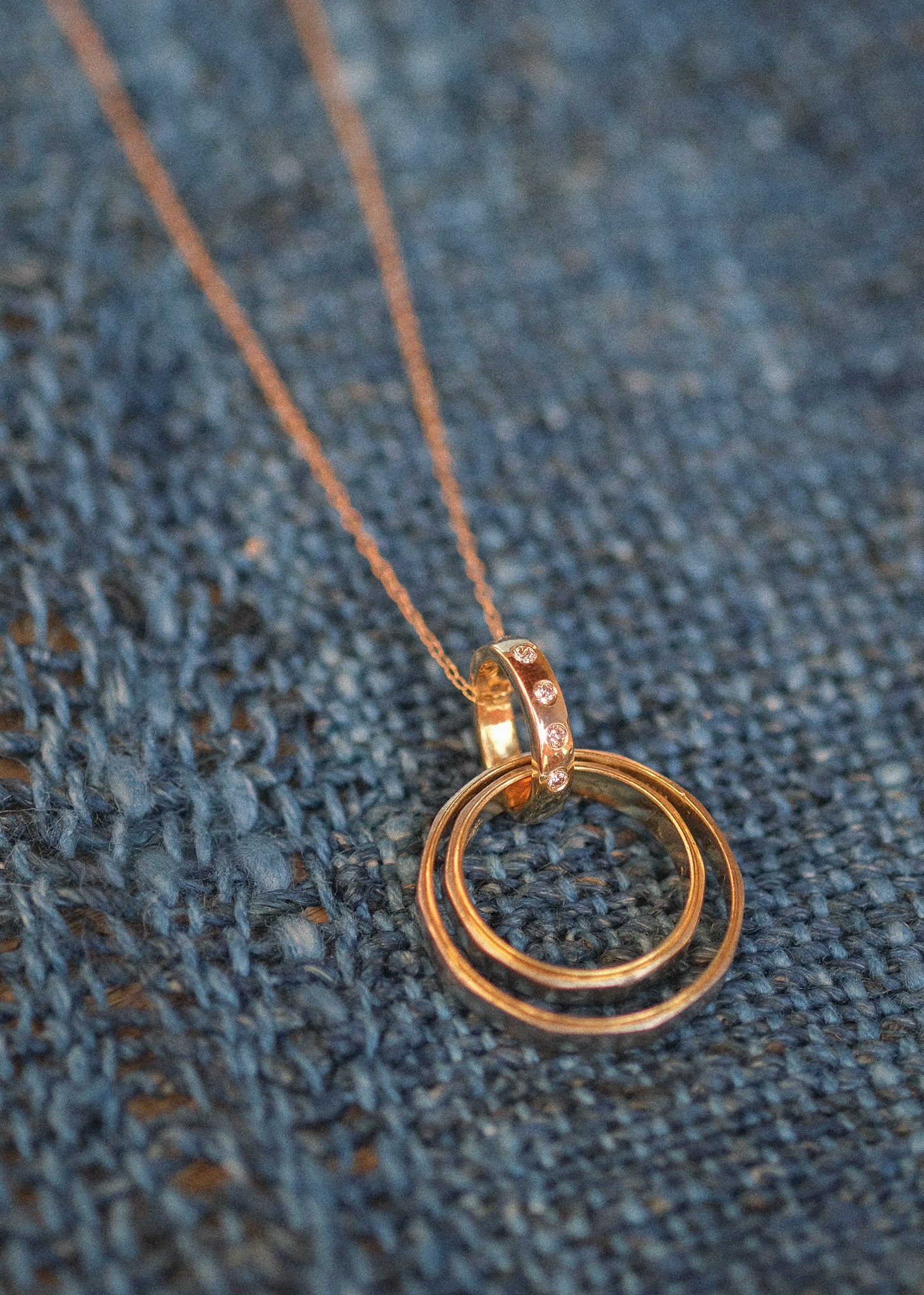 A custom gold necklace with champagne diamonds holding wedding rings. Shown on a linen blue surface.