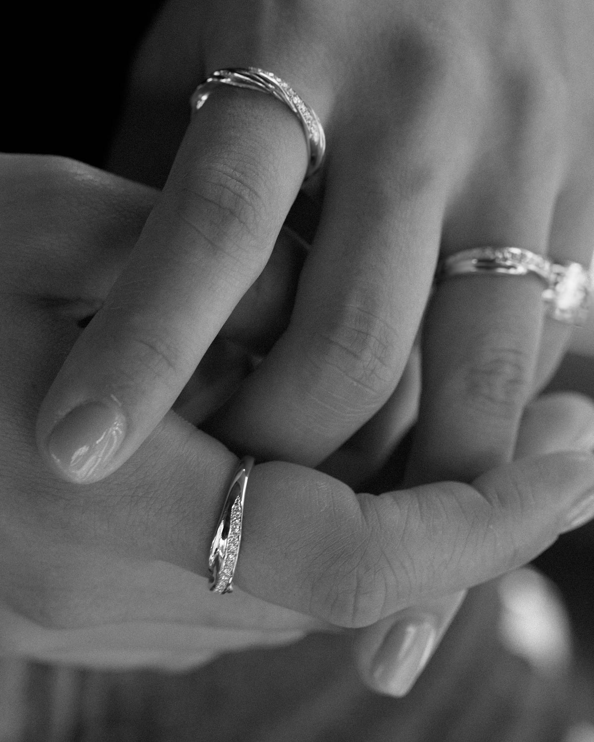 A close-up black and white photograph of a person's hands wearing three 18 karat gold rings, all made using Mitsuro hikime and featuring pavé set diamonds.