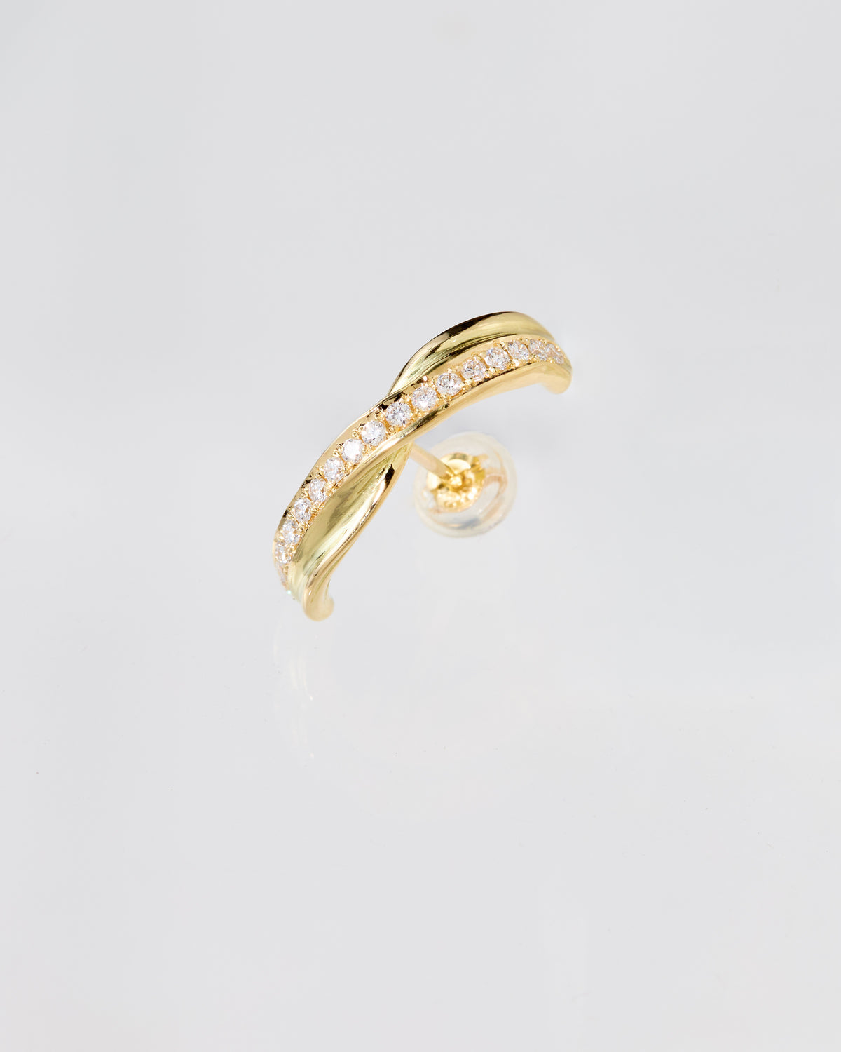 A gold huggie earring with a row of clear pavé diamonds along one band, shown on a clean light gray background with the clear backing visible behind it.