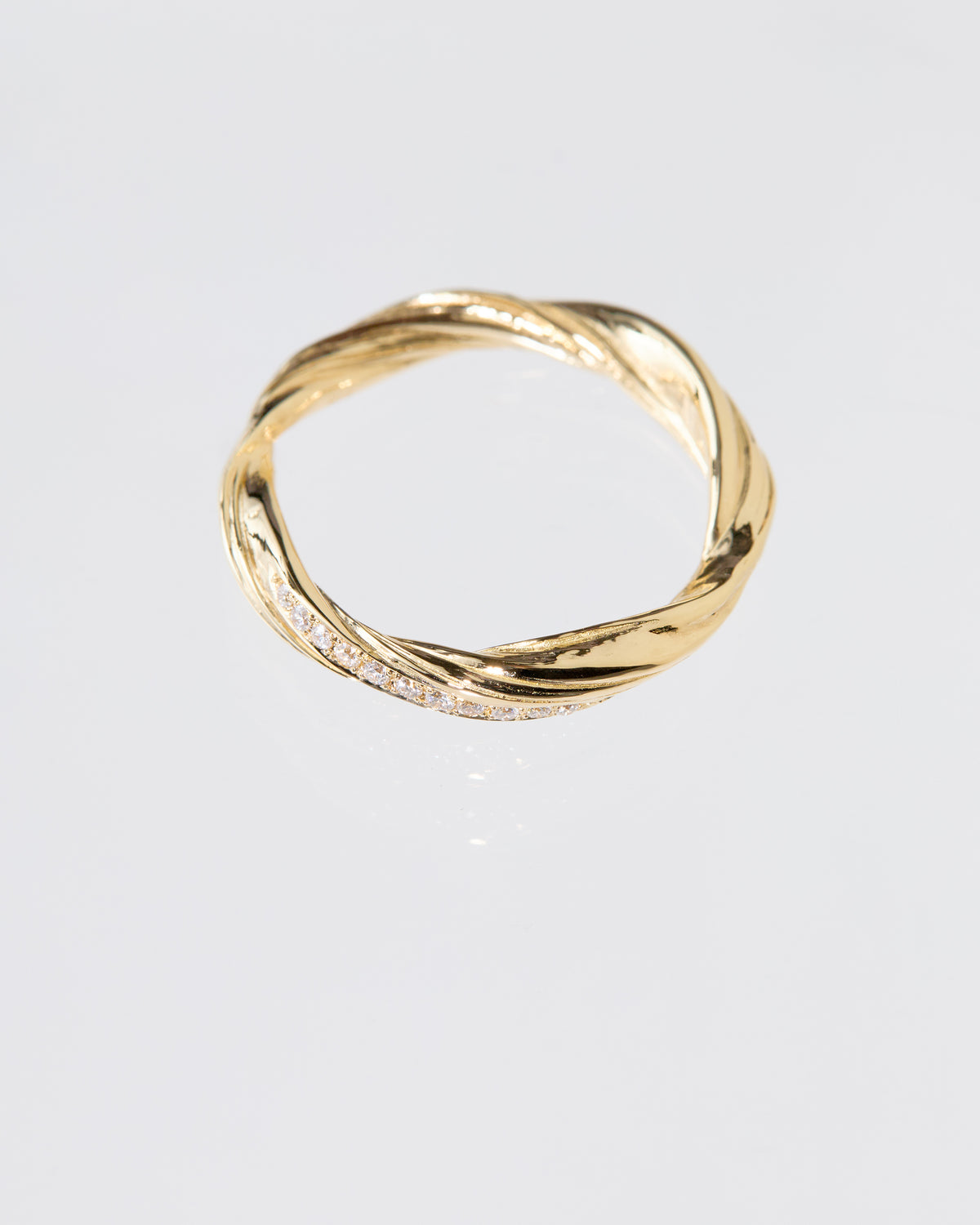 A twisted gold band ring with a row of pavé diamonds along one side, photographed on a clean light gray background.