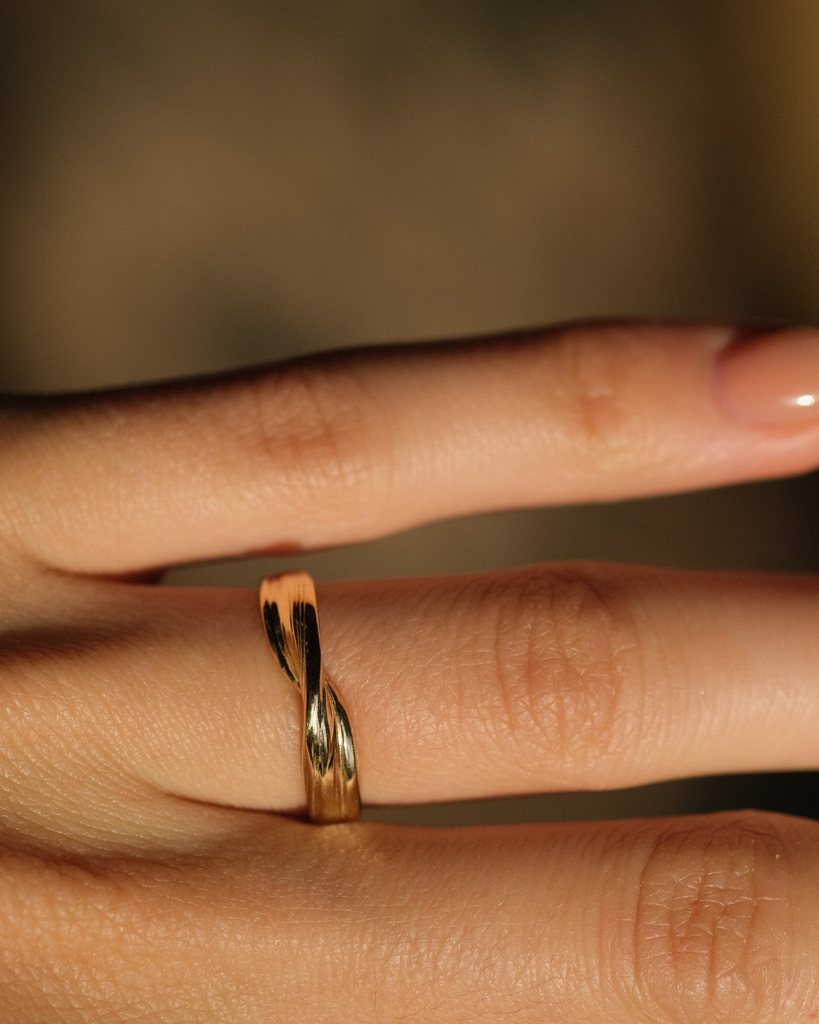 18k gold twisting wedding ring on a finger with a blurred background