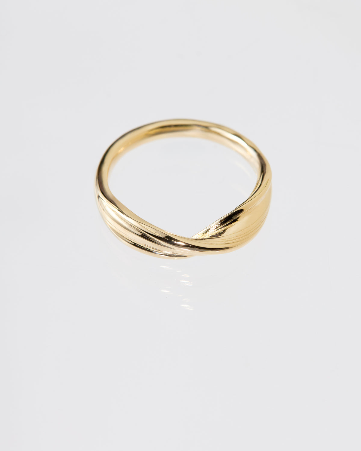 A polished gold ring with a twisted, fluid Mitsuro hikime design, photographed on a clean light gray reflective surface.
