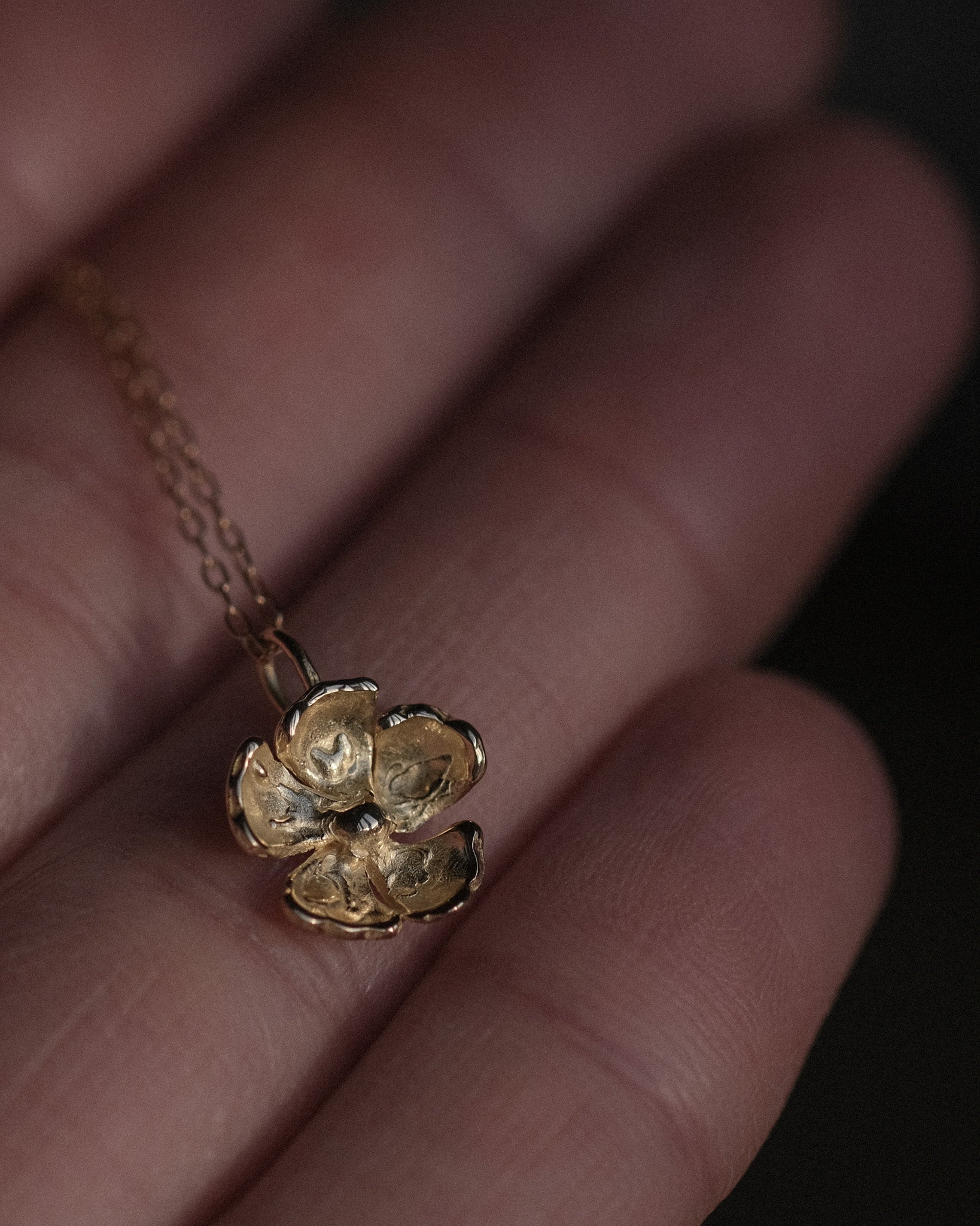 Gold necklace with a flower pendant held in a hand against a blurred background
