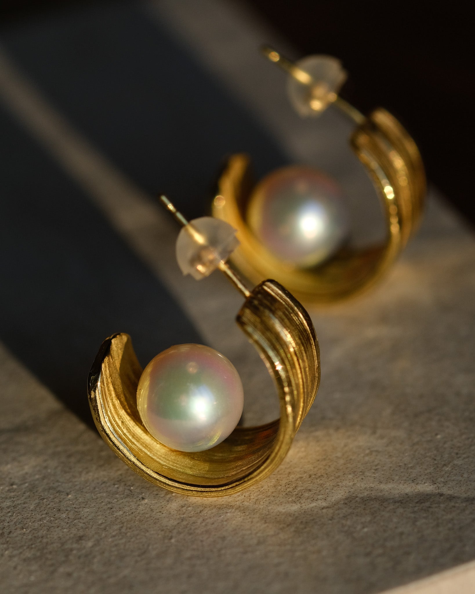 Gold hoop earrings with pearl centers on a textured surface