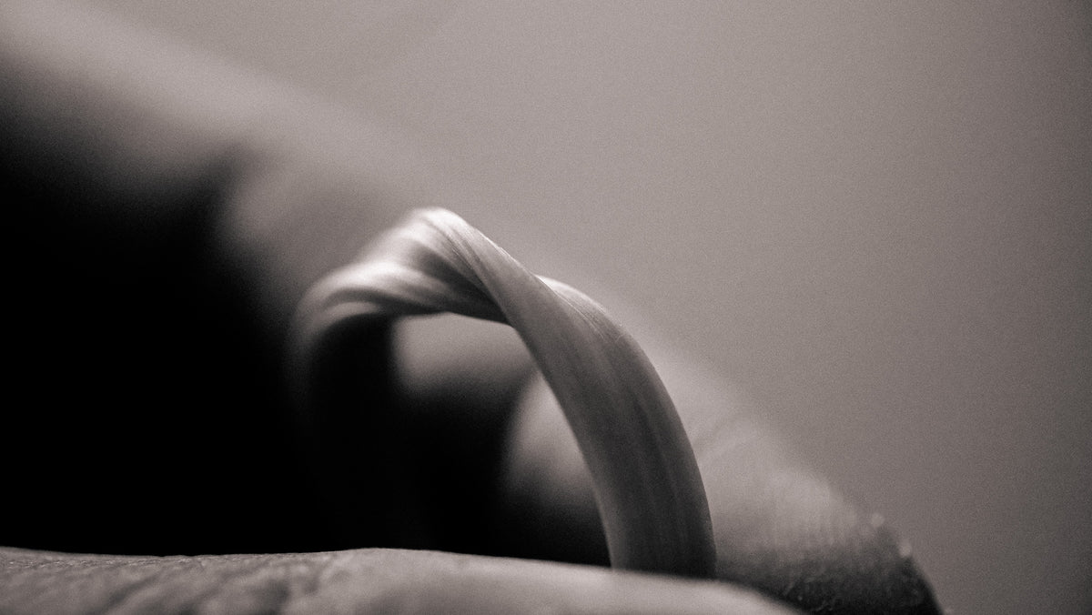 A close-up of a hand holding a twisted, ribbon-like mitsuro hikime ring against a soft beige background.