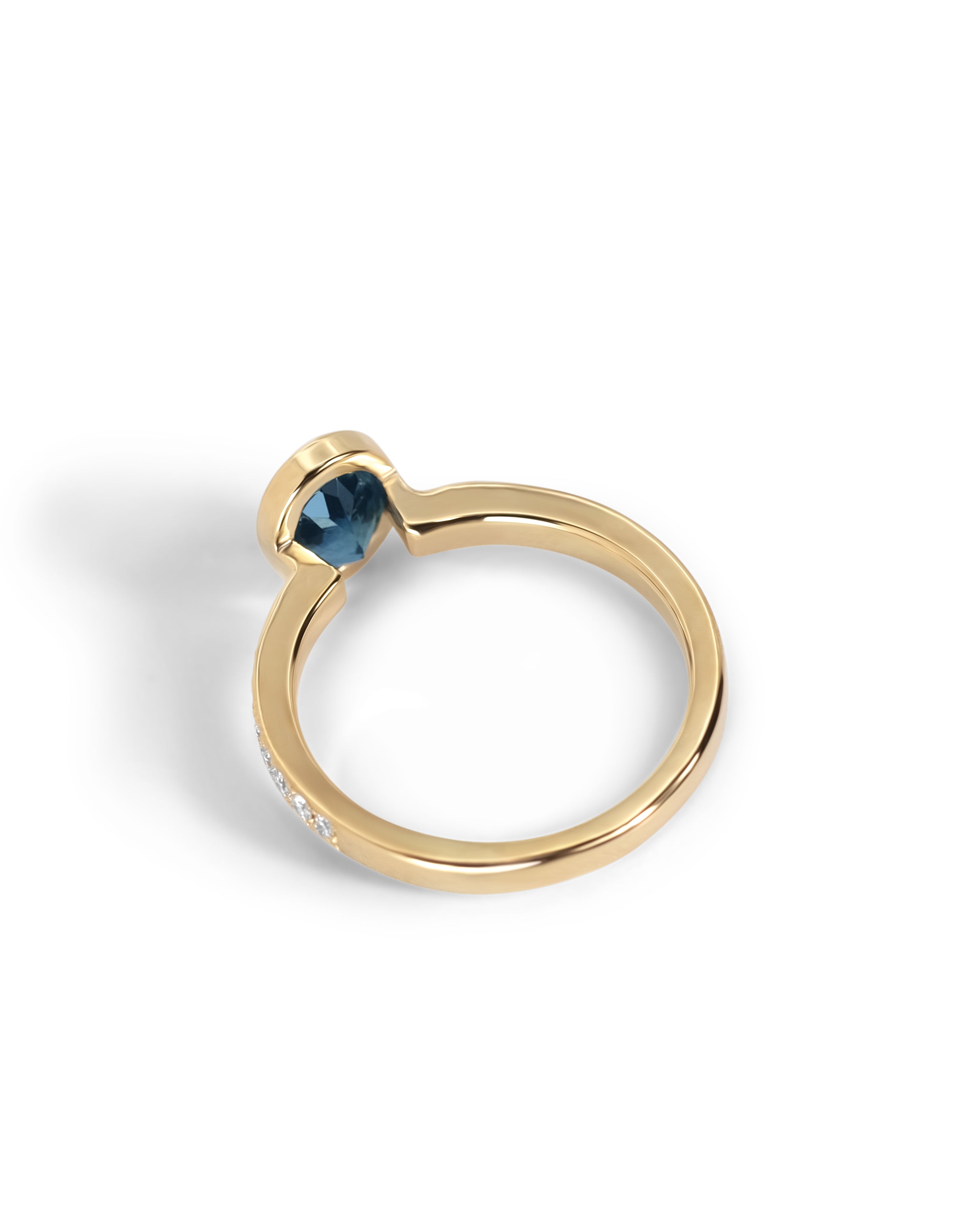A gold engagement ring featuring a Montana Sapphire in a bezel setting, with a row of diamonds, shown on a white background with a soft shadow.