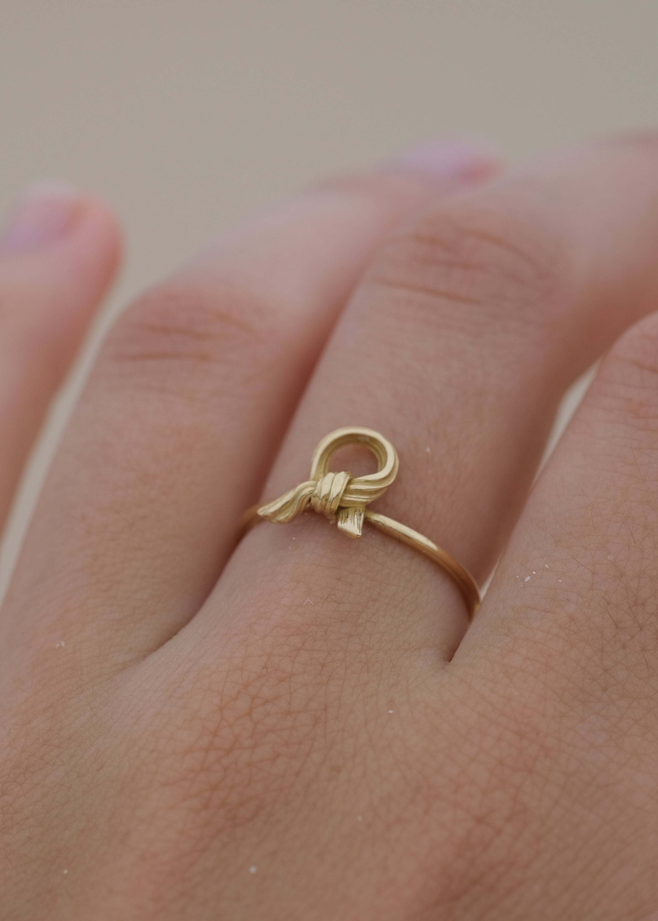 Gold ring with a knot design on a hand against a neutral background