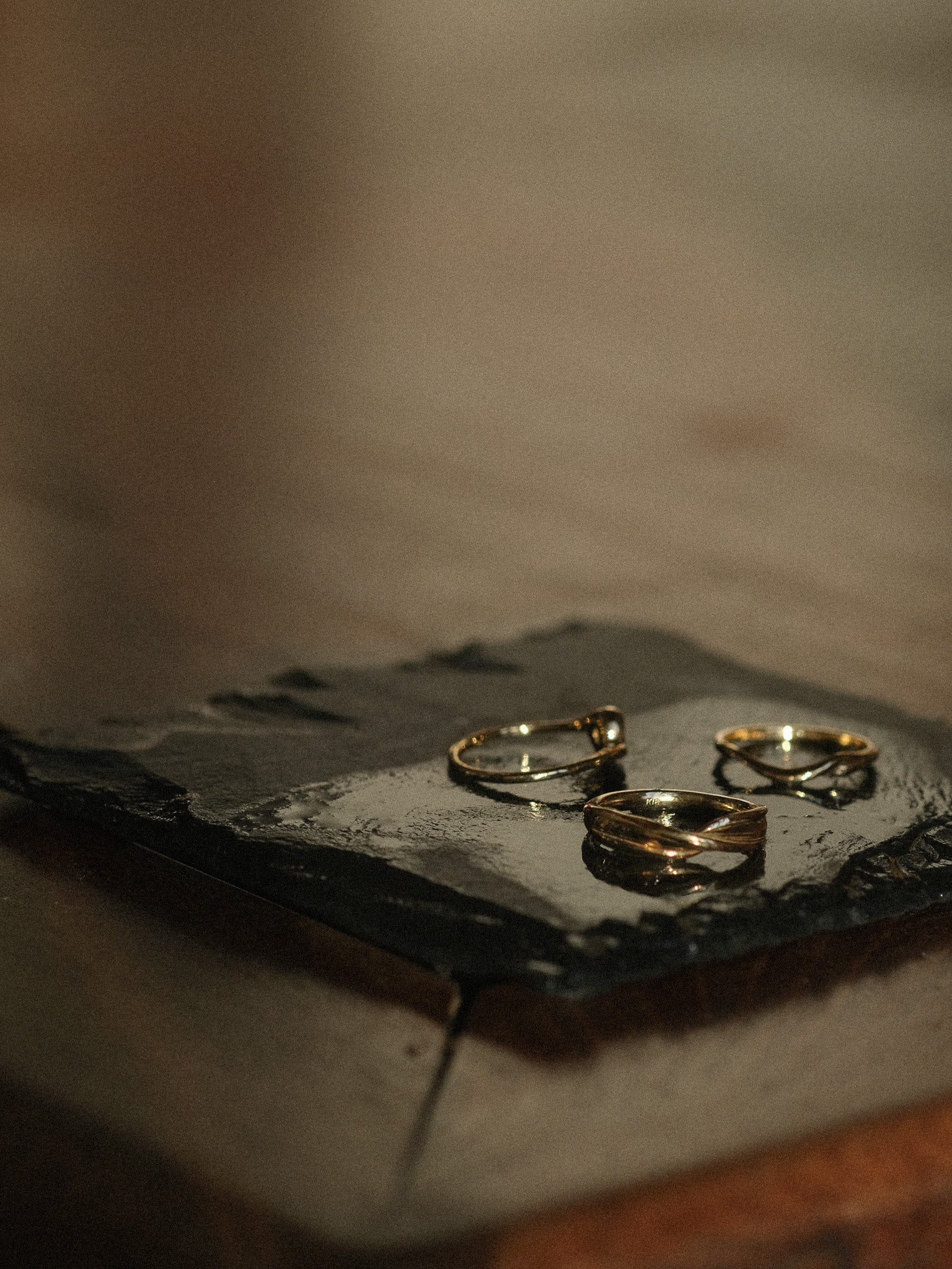 Three gold rings on a dark stone surface with a blurred background