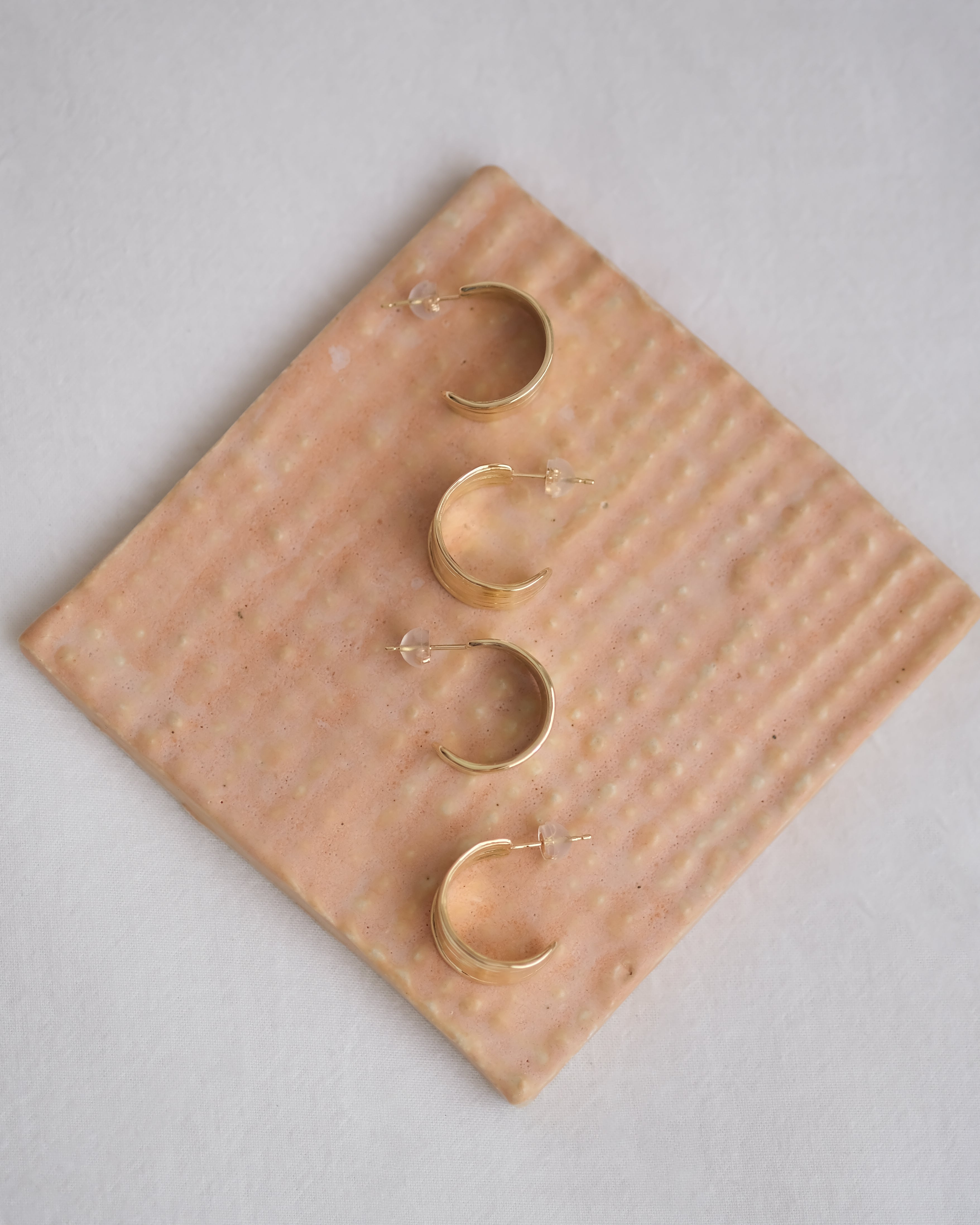 Set of gold hoop earrings on a textured beige stone surface