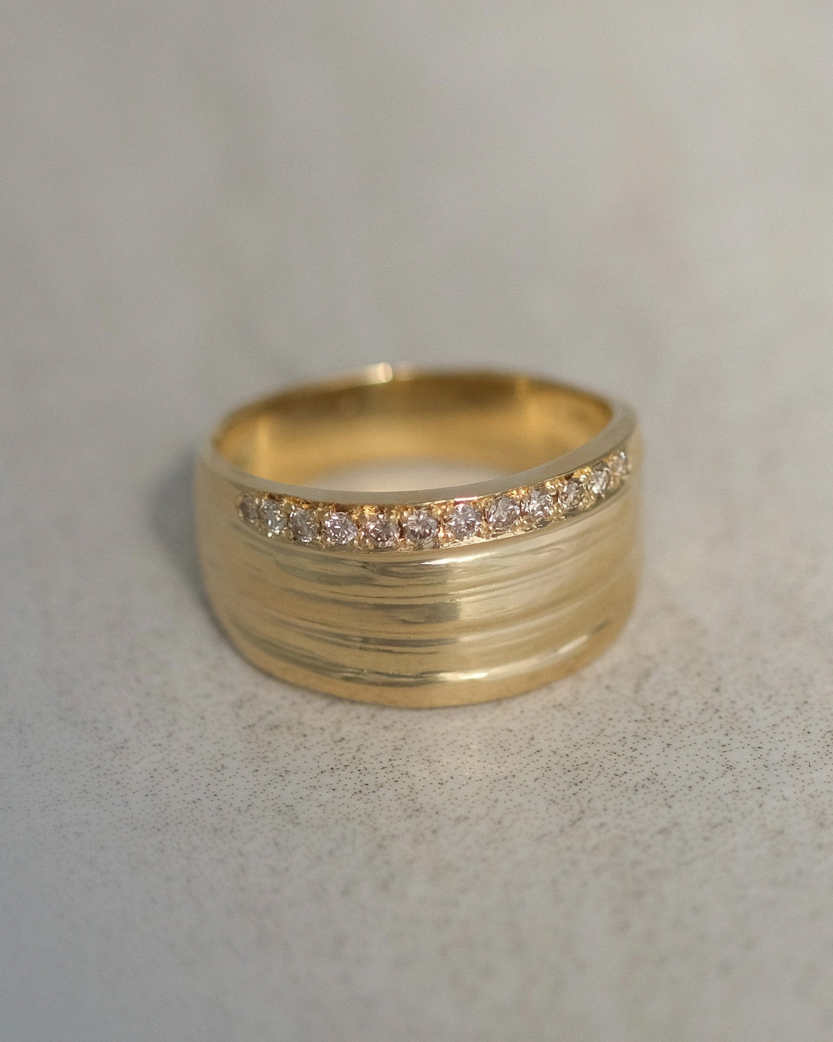 A handcrafted 18k gold pinky ring featuring a row of small champagne diamonds across the front, set against a neutral light gray background.