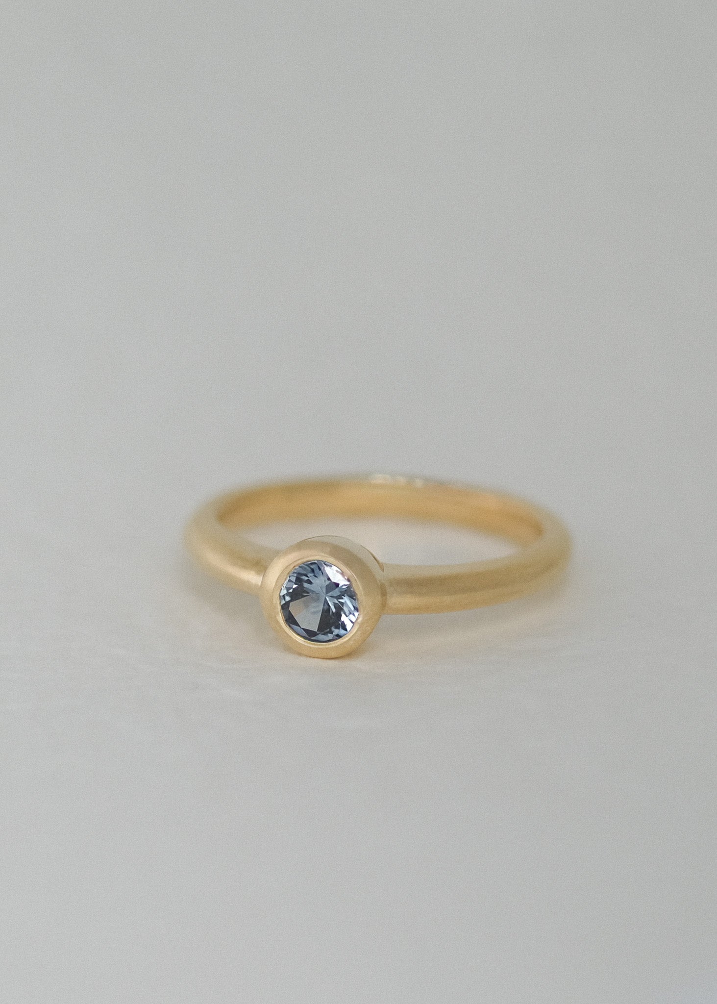 A natural, unheated Montana sapphire in a bezel setting, photographed against a soft, light gray background. A handcrafted and unique engagement ring made in Karuizawa, Japan.