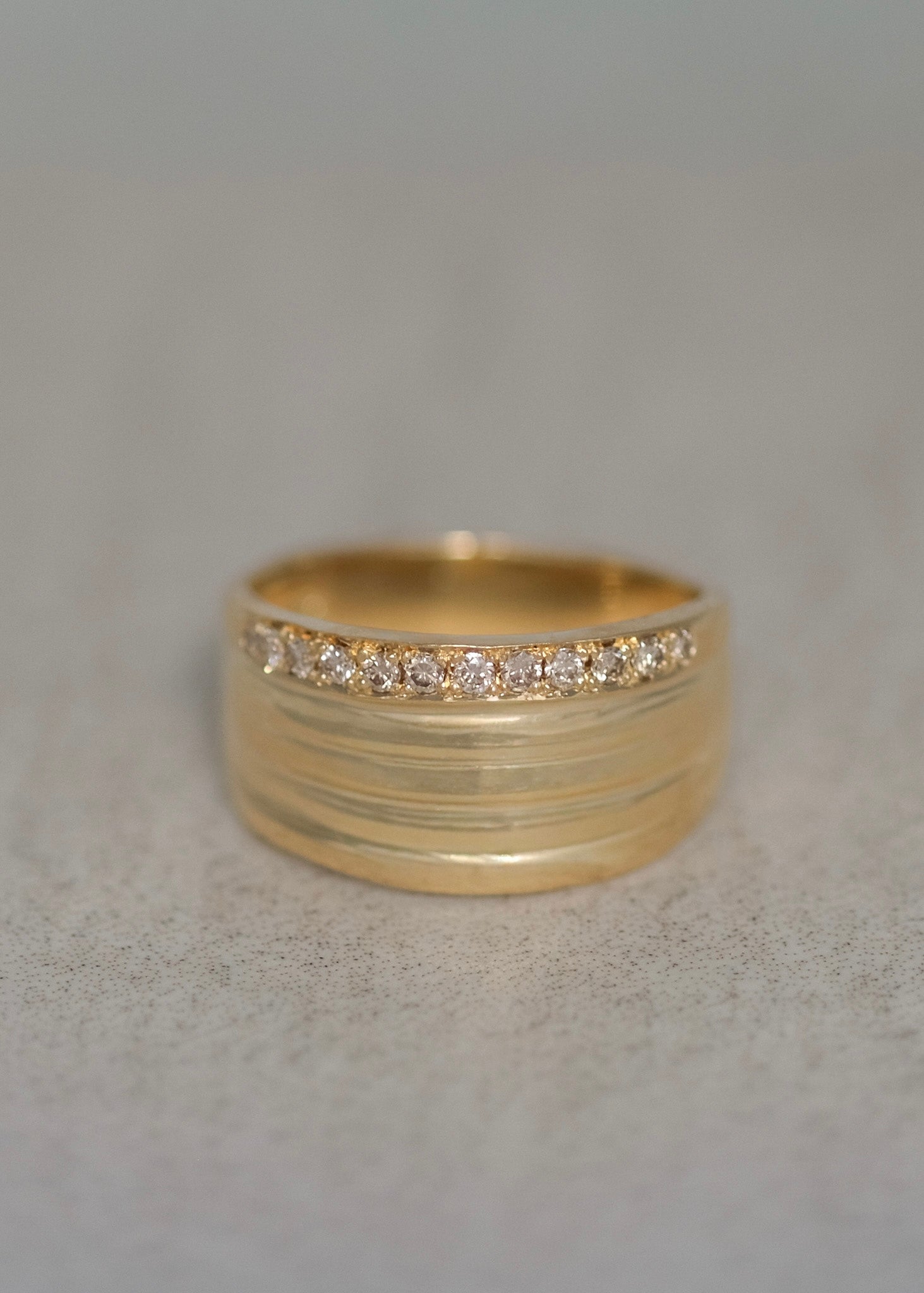 A handcrafted 18k gold pinky ring featuring a row of small champagne diamonds across the front, set against a neutral light gray background.