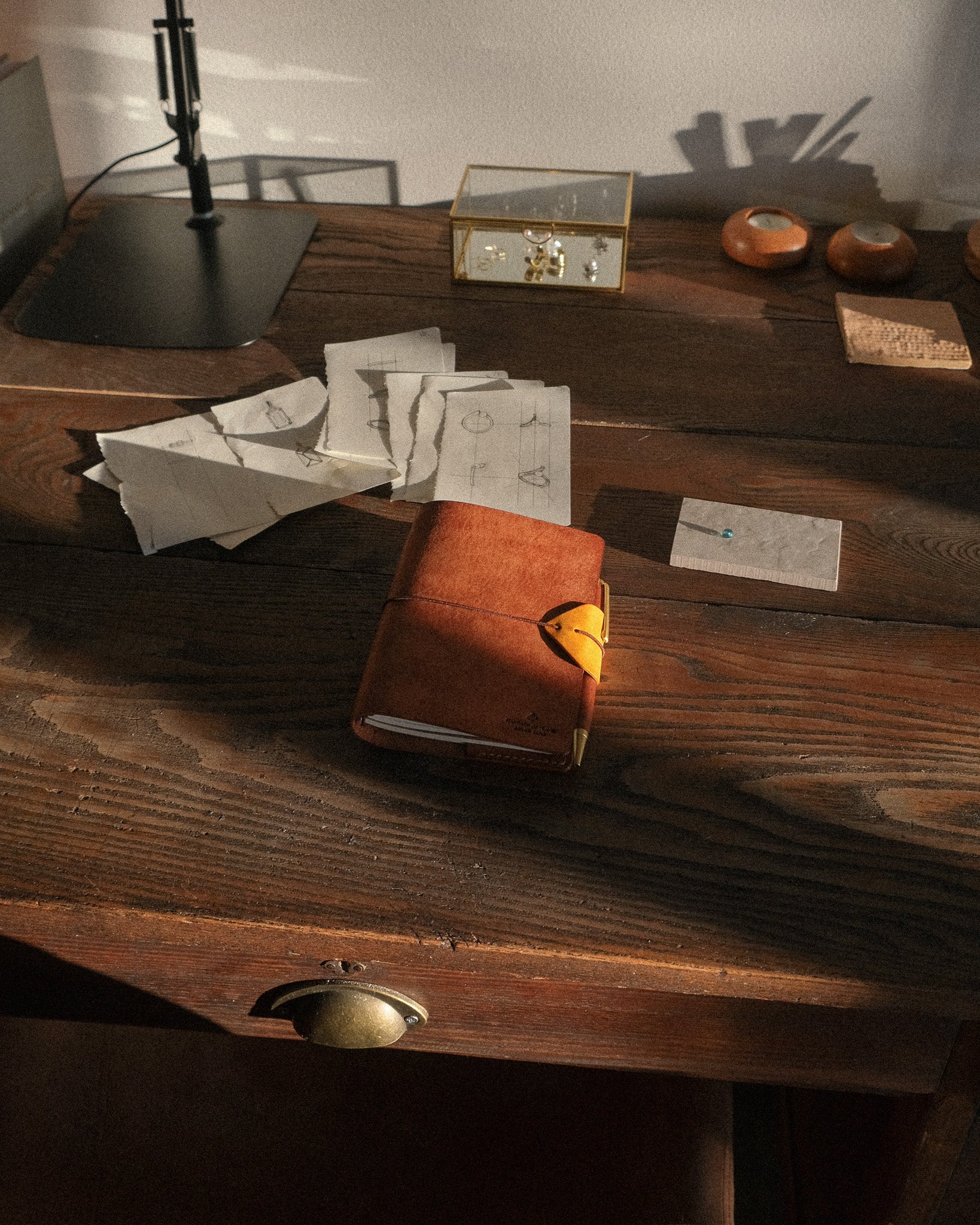 Vintage desk with leather-bound book, papers, and small objects on a wooden surface.