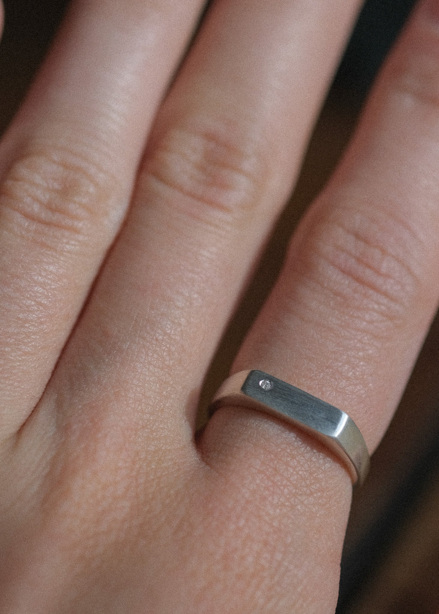 A close-up of a hand wearing a minimalist silver signet ring with a tiny diamond flush set.