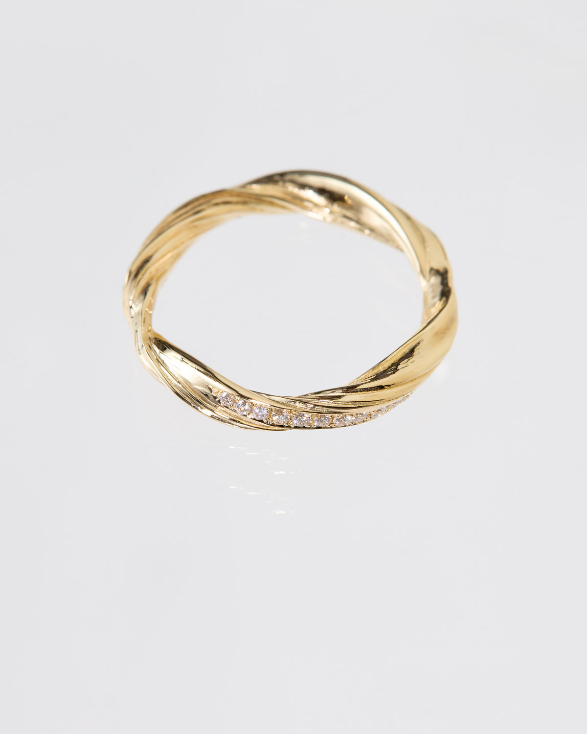 A twisted gold band ring with a row of pavé diamonds along one side, photographed on a clean light gray background.