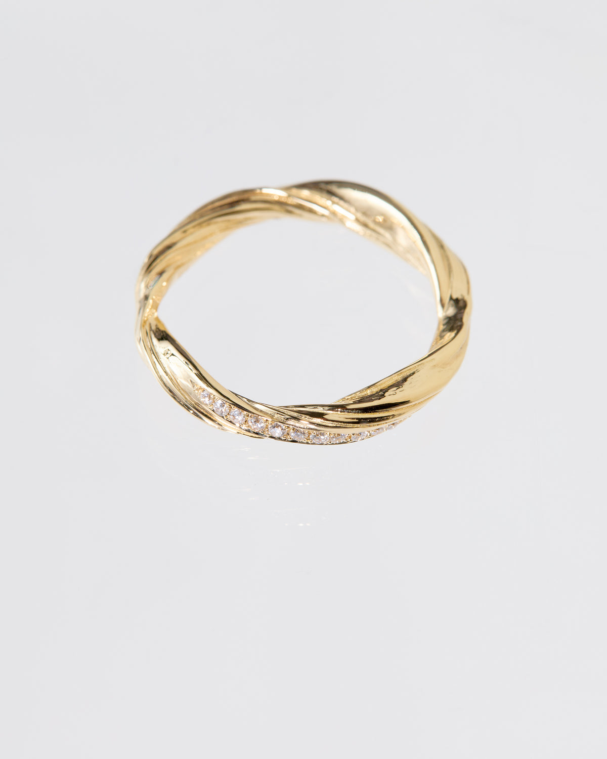A twisted gold band ring with a row of pavé diamonds along one side, photographed on a clean light gray background.