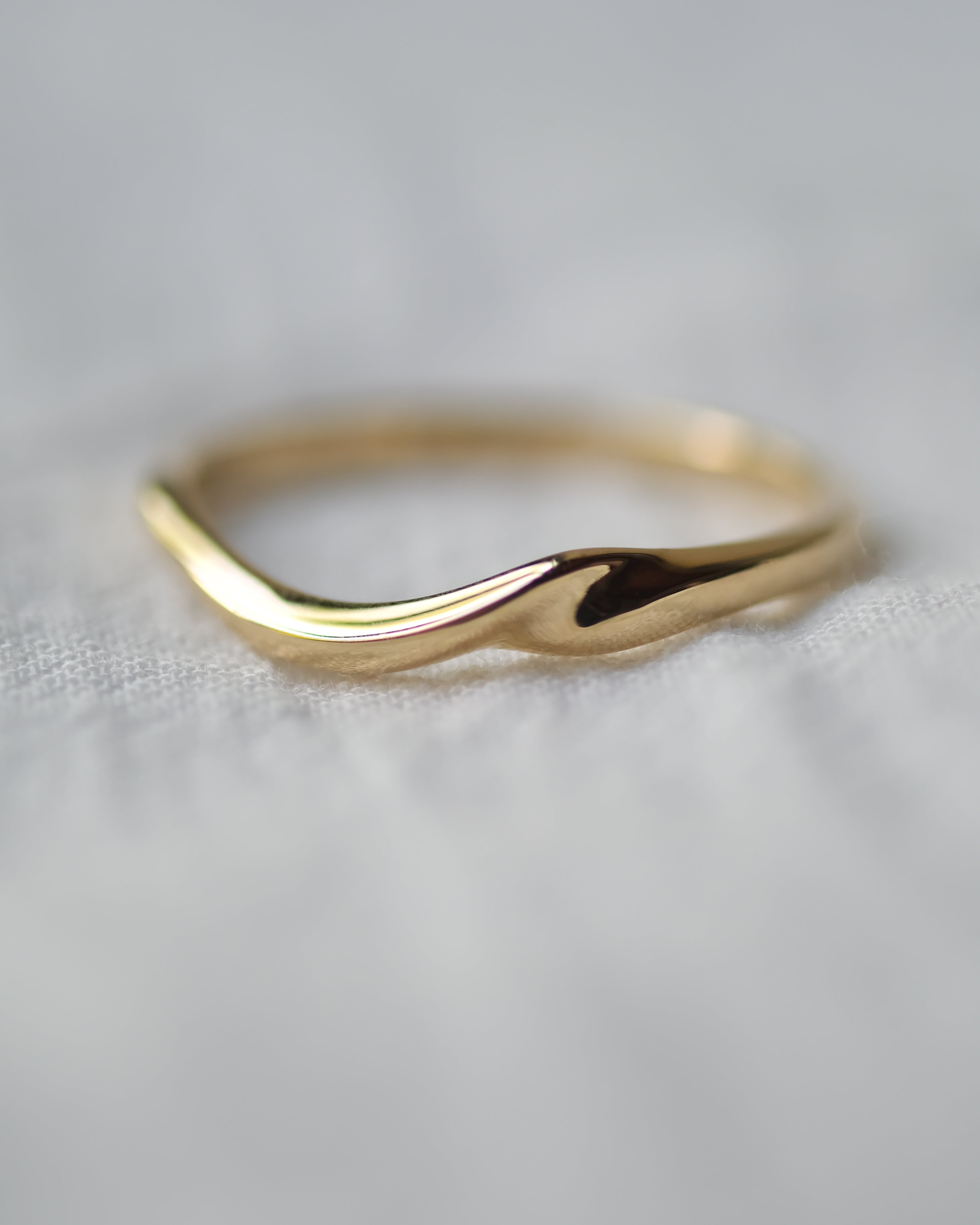 Gold ring with a wavy design on a light gray background