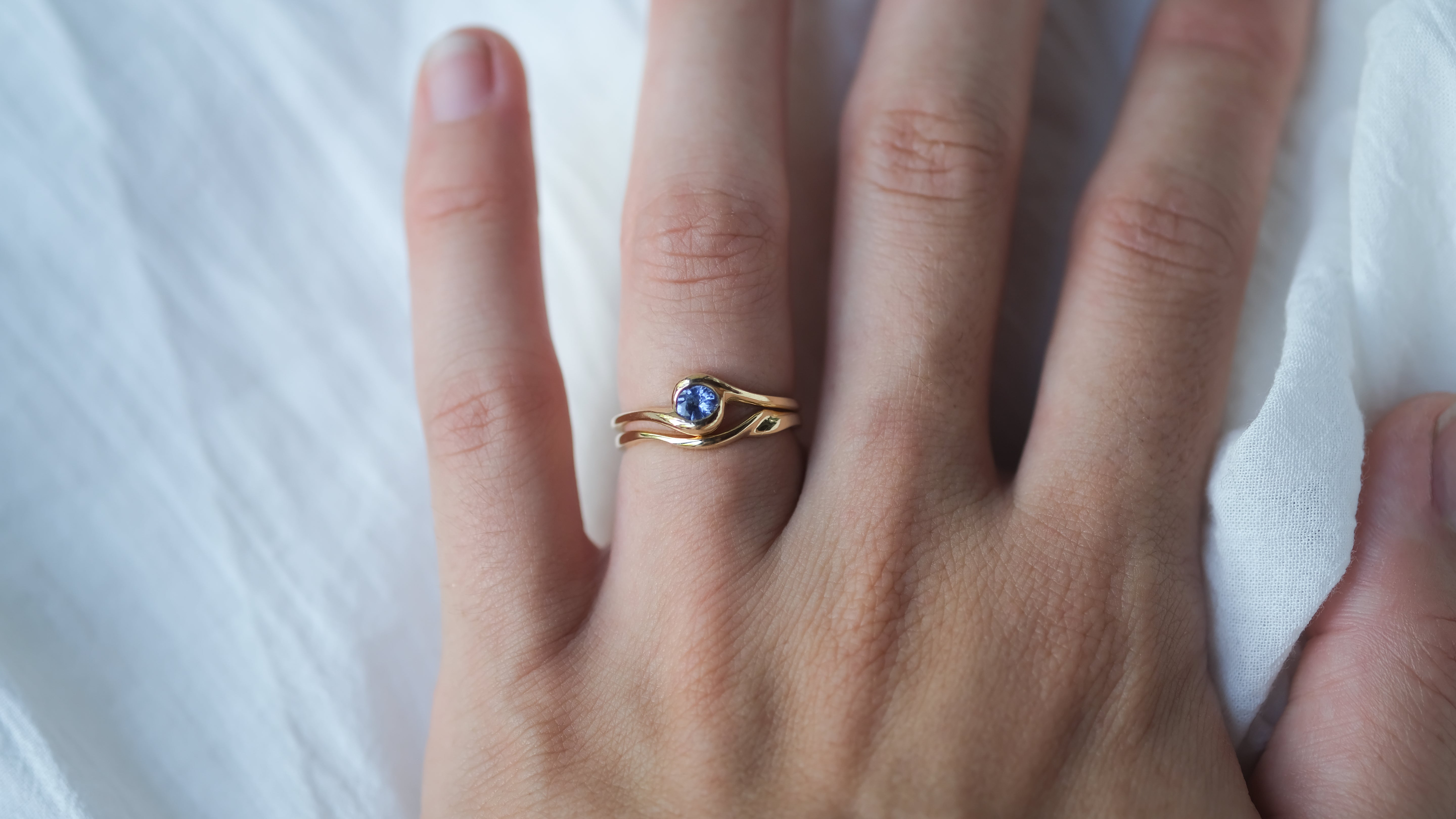 Hand wearing a gold ring with a blue gemstone on a white background