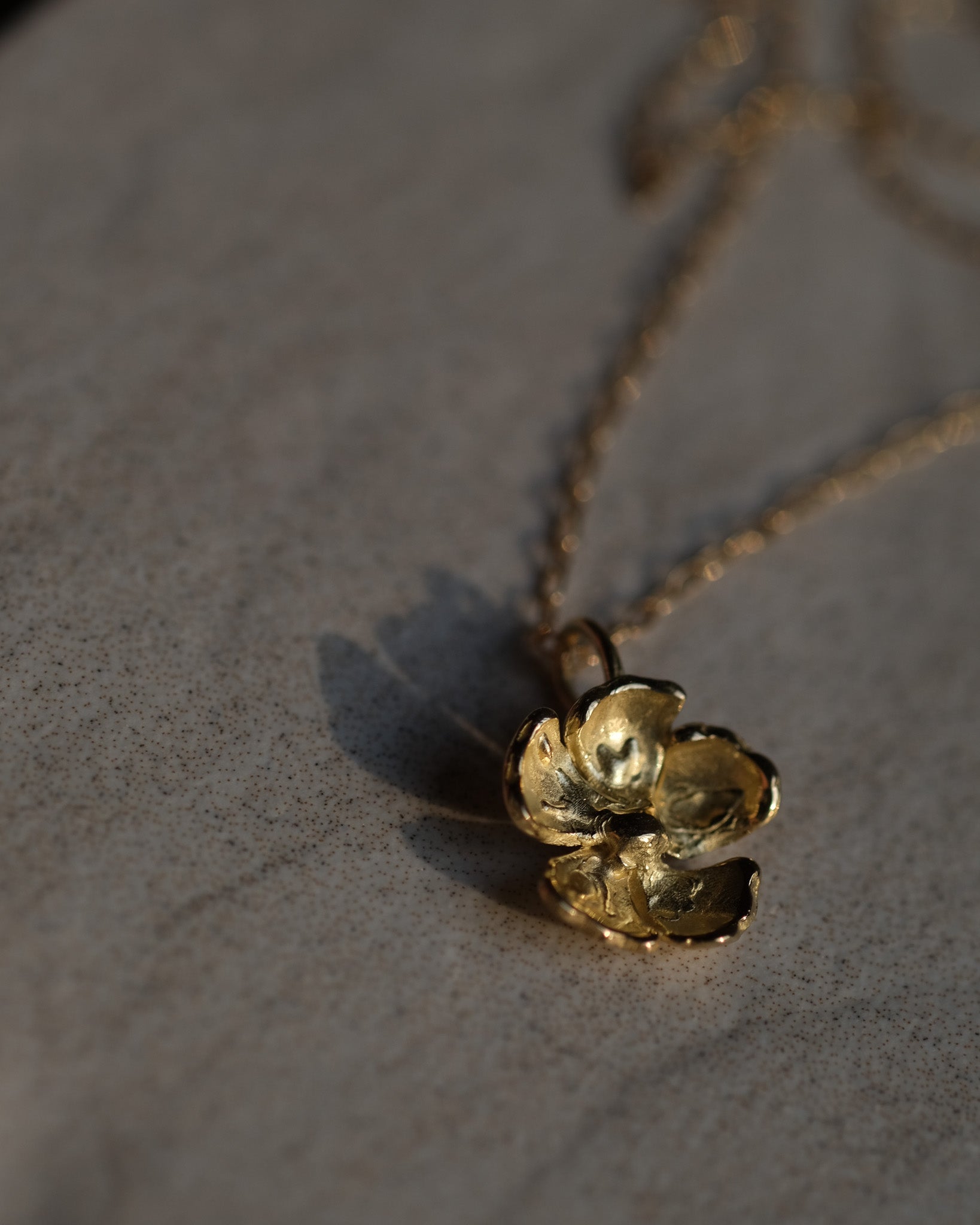 Gold flower-shaped pendant on a chain against a neutral background