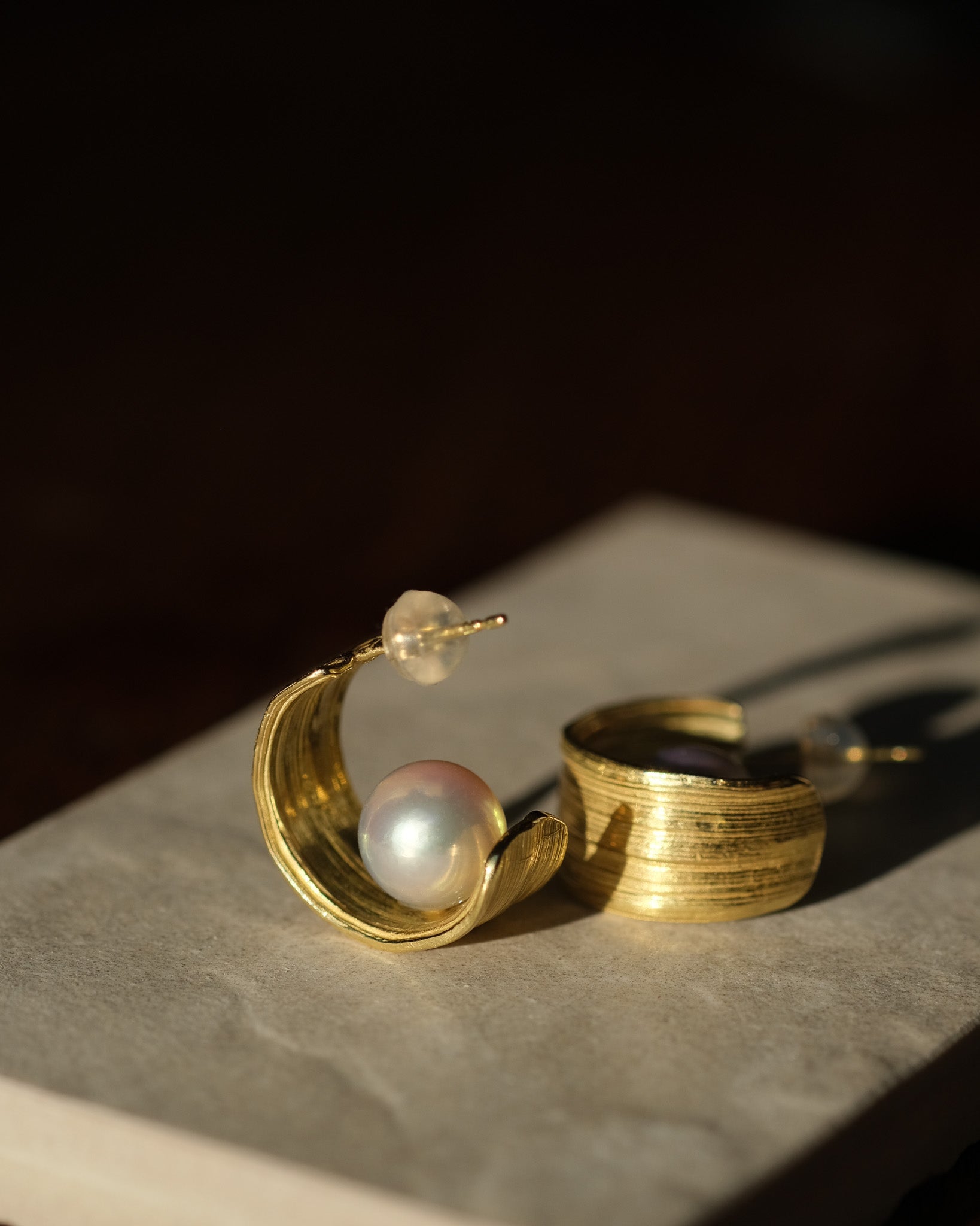 Gold hoop earrings with pearls on a dark surface