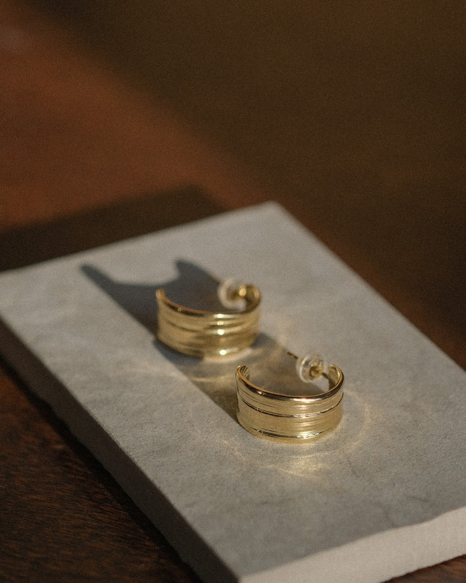 Gold hoop earrings on a gray stone surface with a blurred background