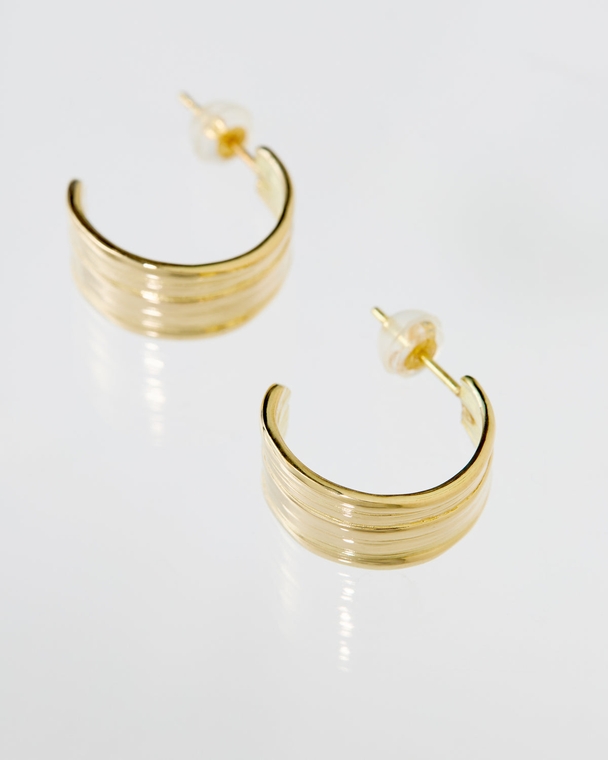 A pair of gold crescent hoop earrings with streaming Mitsuro hikime texture displayed on a clean white reflective surface.