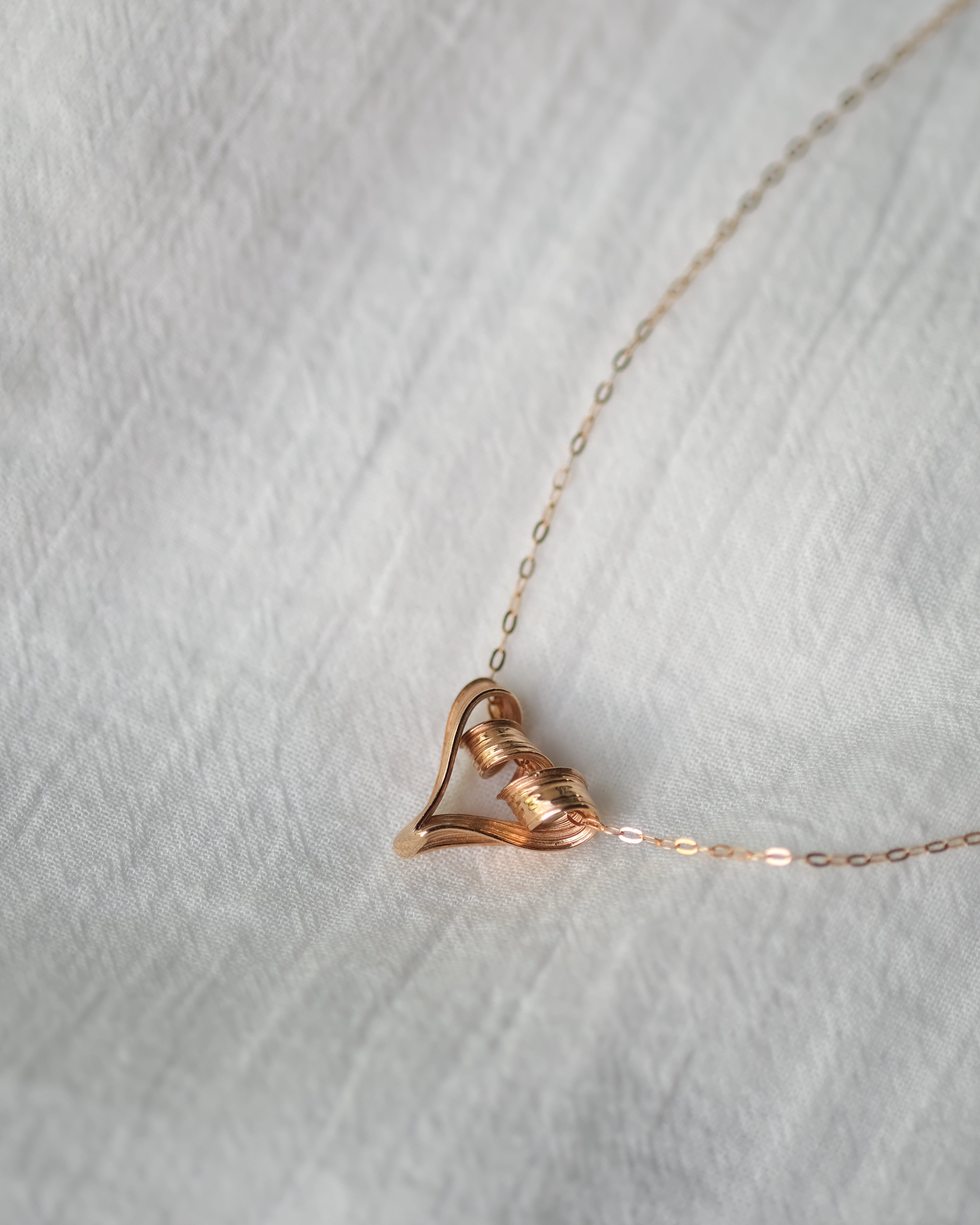 Rose gold necklace with a heart-shaped pendant on a light gray background