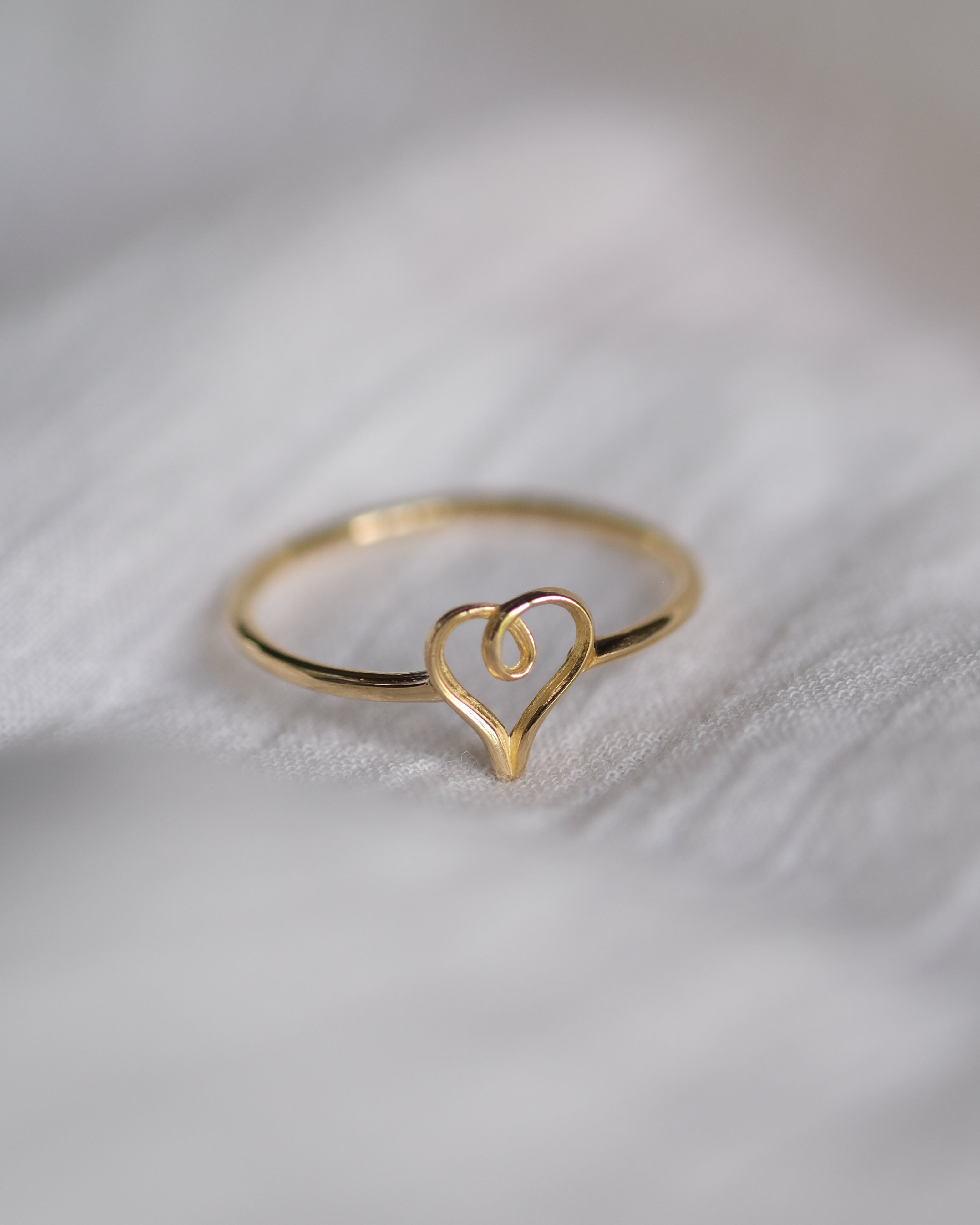 Gold heart-shaped ring on a soft white fabric background