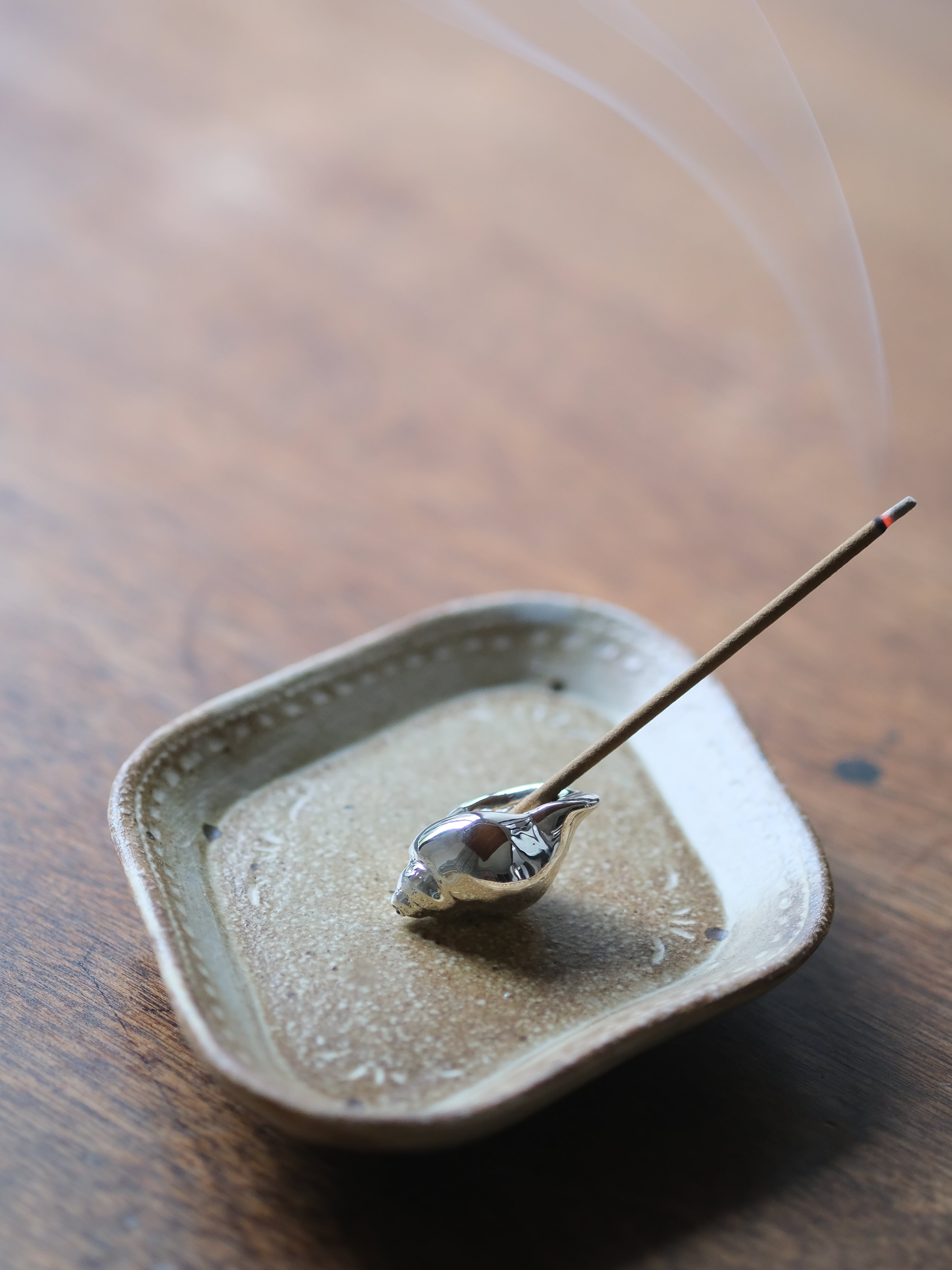 Incense stick on a ceramic dish with smoke on a wooden surface