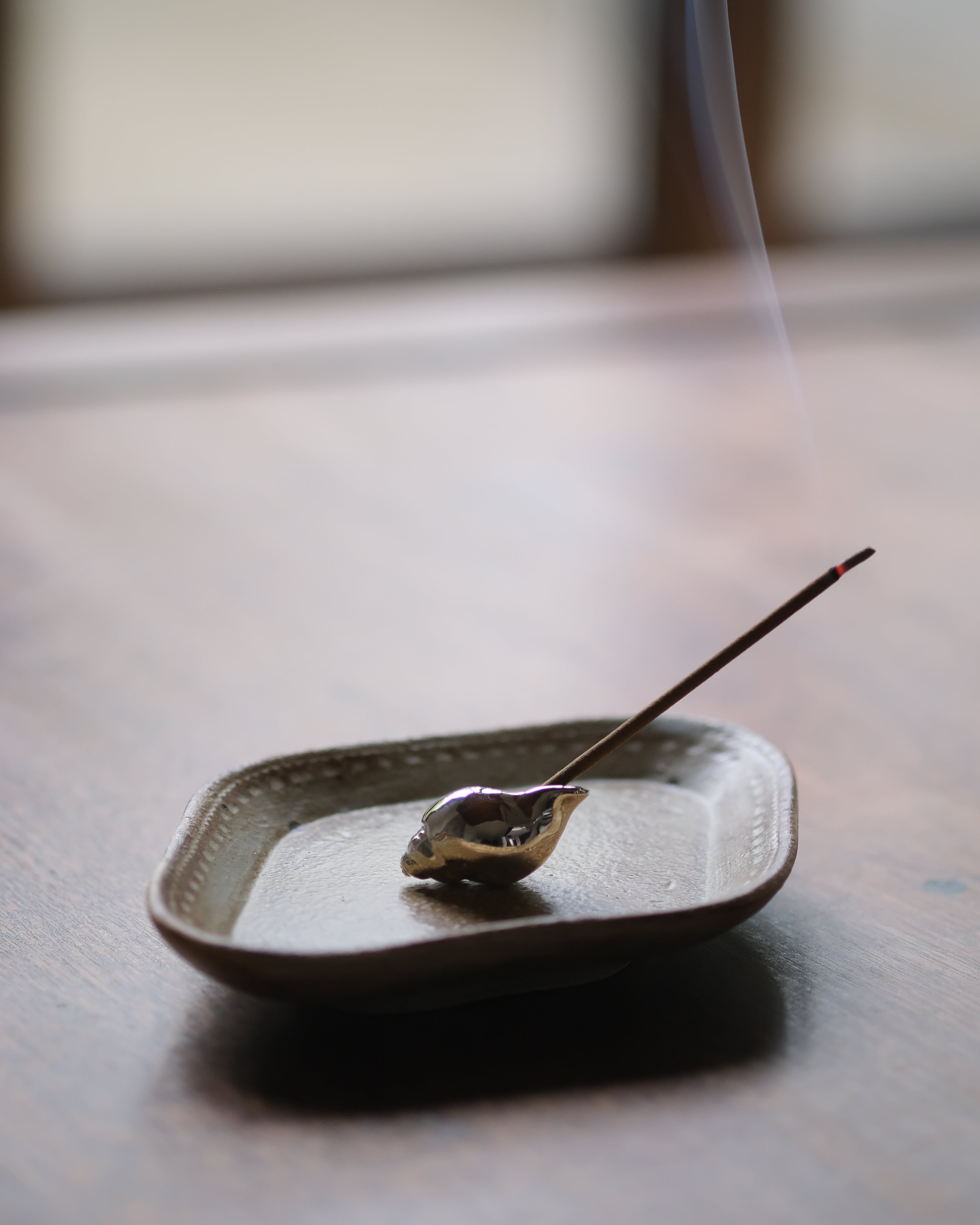 Incense stick on a small ceramic dish with smoke rising, on a wooden surface.