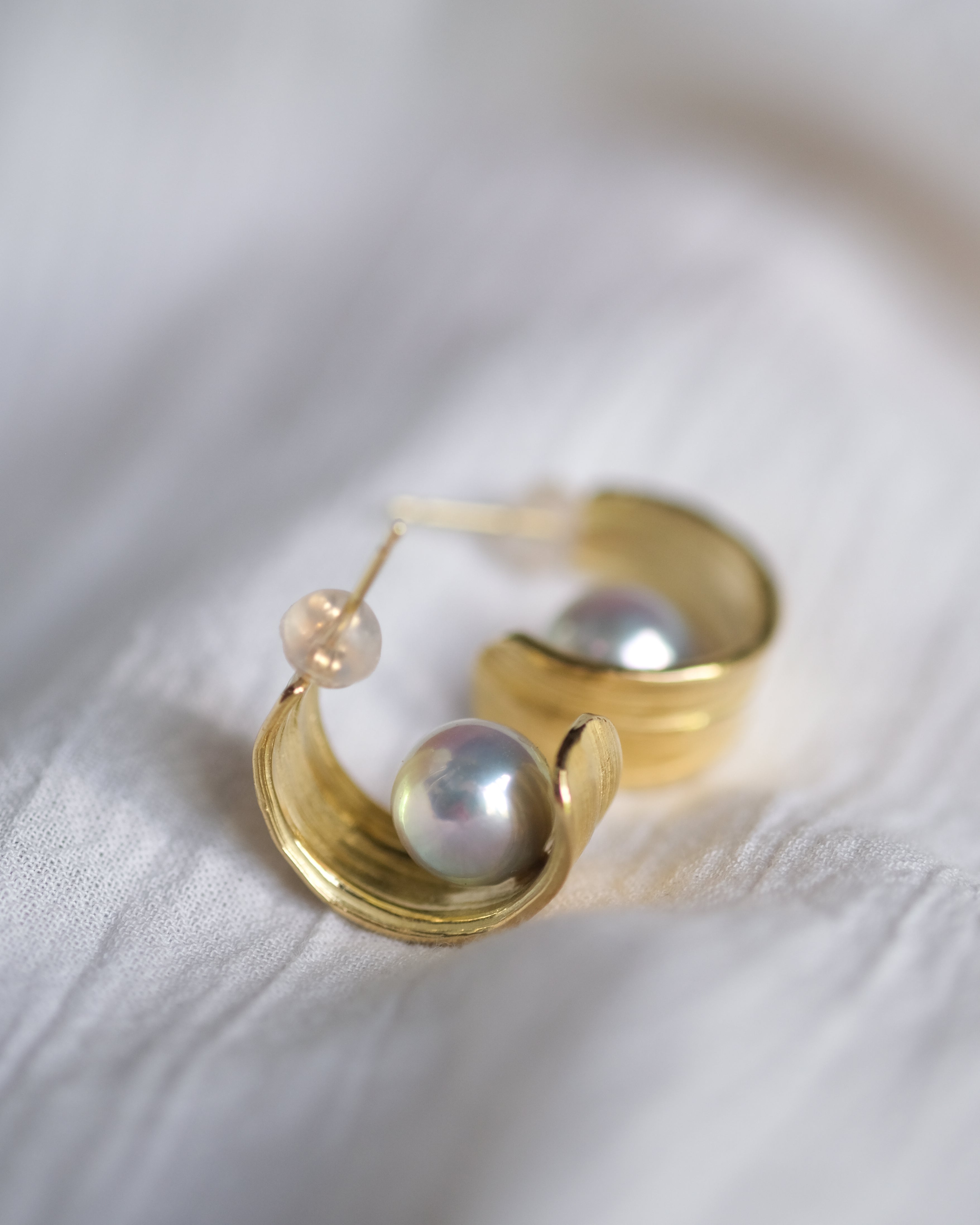 Gold hoop earrings with pearls on a white fabric background