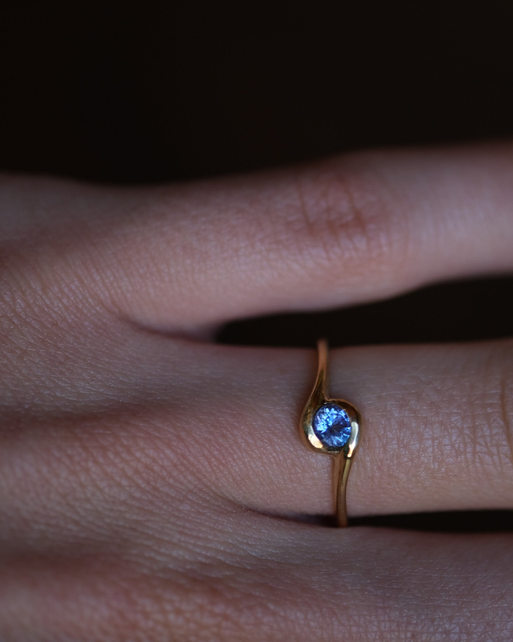 Gold ring with a blue tanzanite on a finger against a dark background