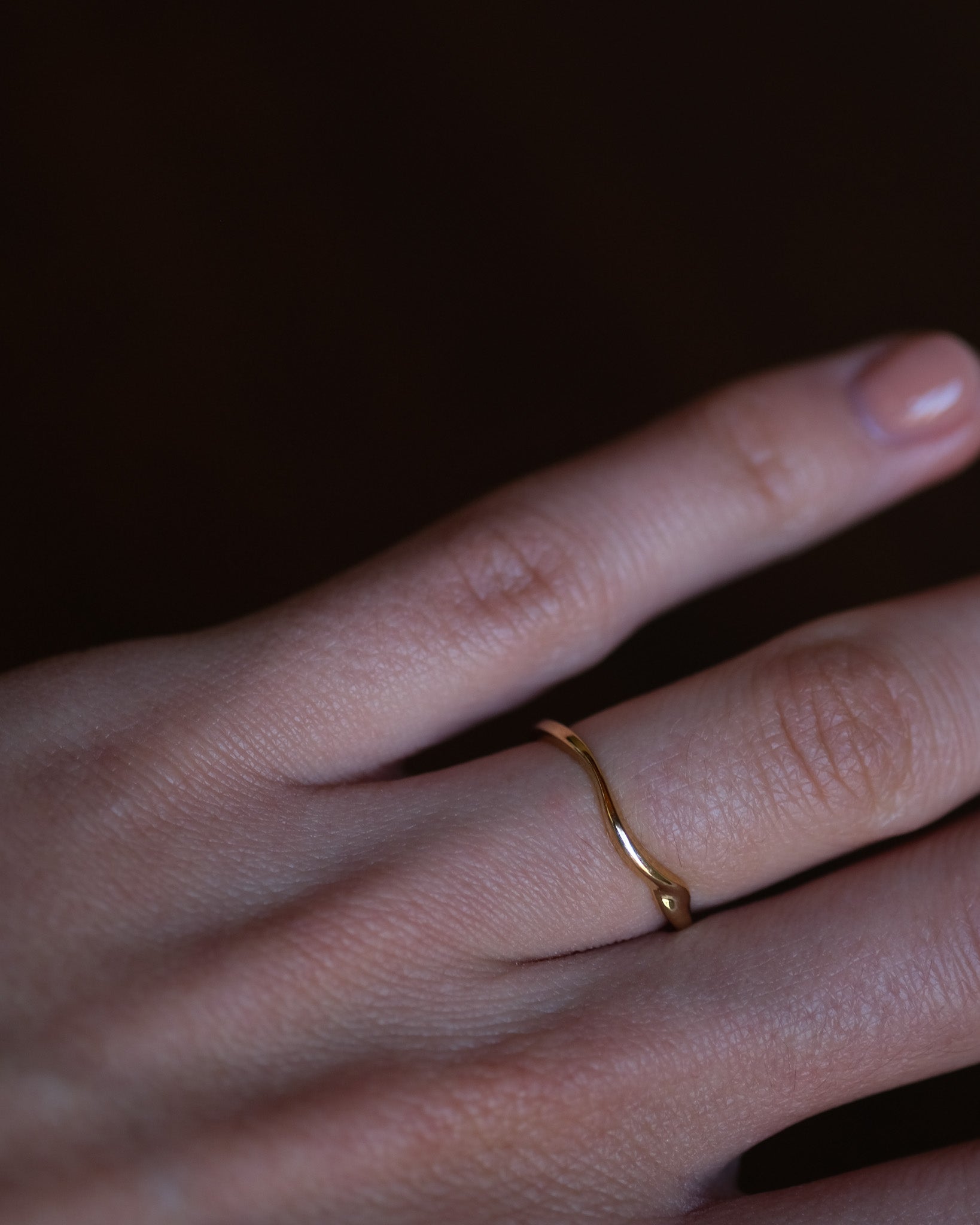 Wavy gold ring on a person's finger against a dark background