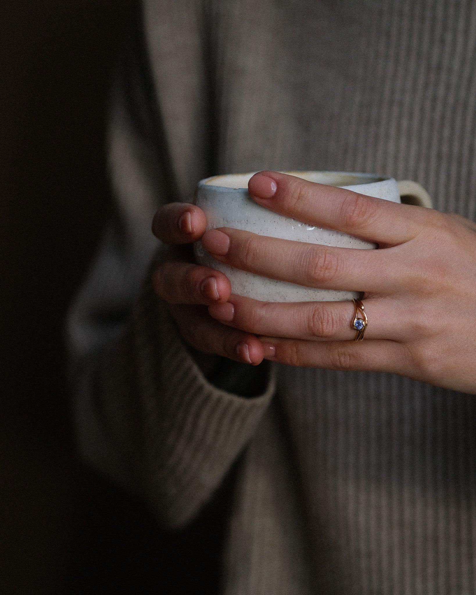 Person holding a white mug and wearing The Yu Duo with a blurred background