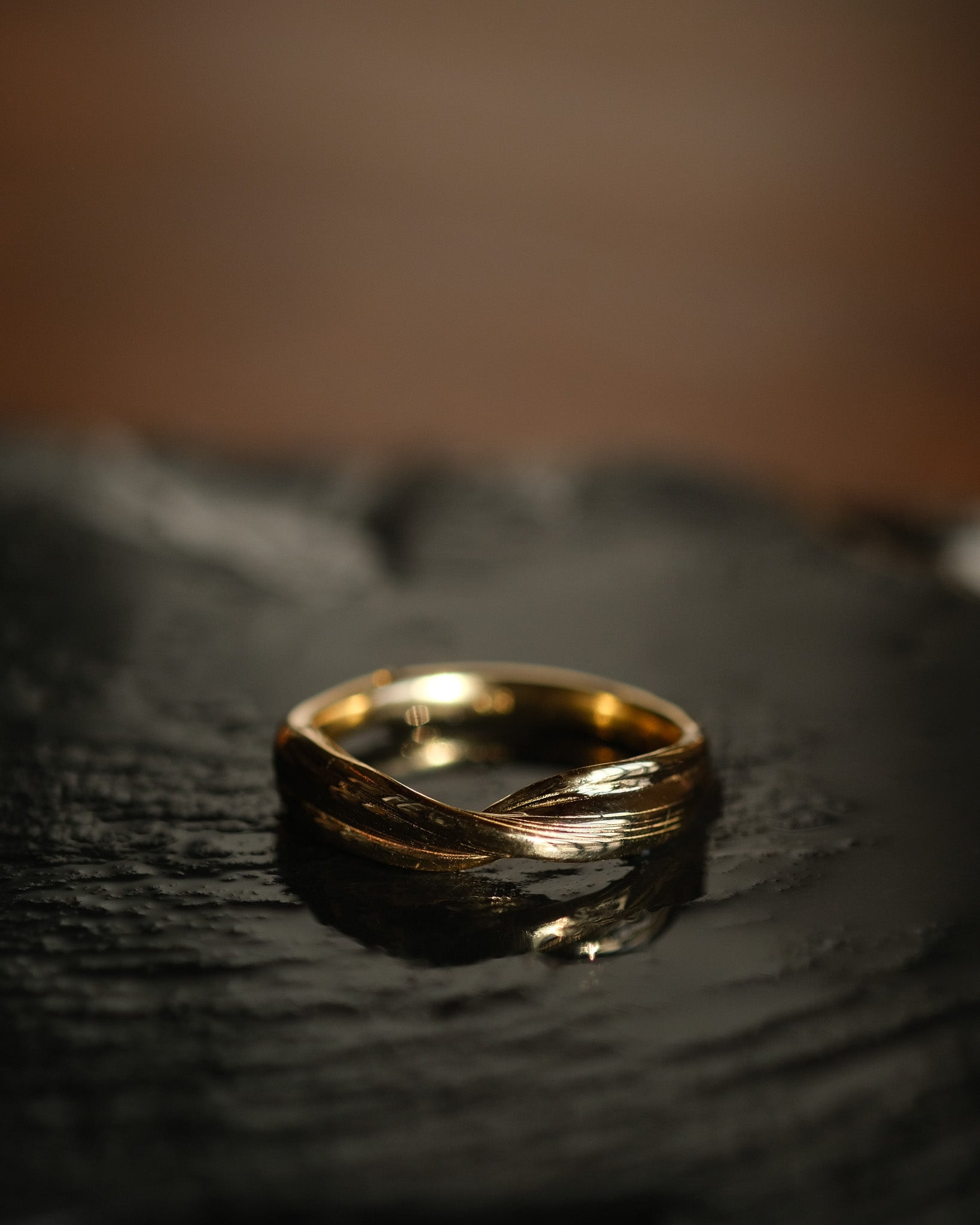 Twisting gold ring on a dark textured surface with a blurred background