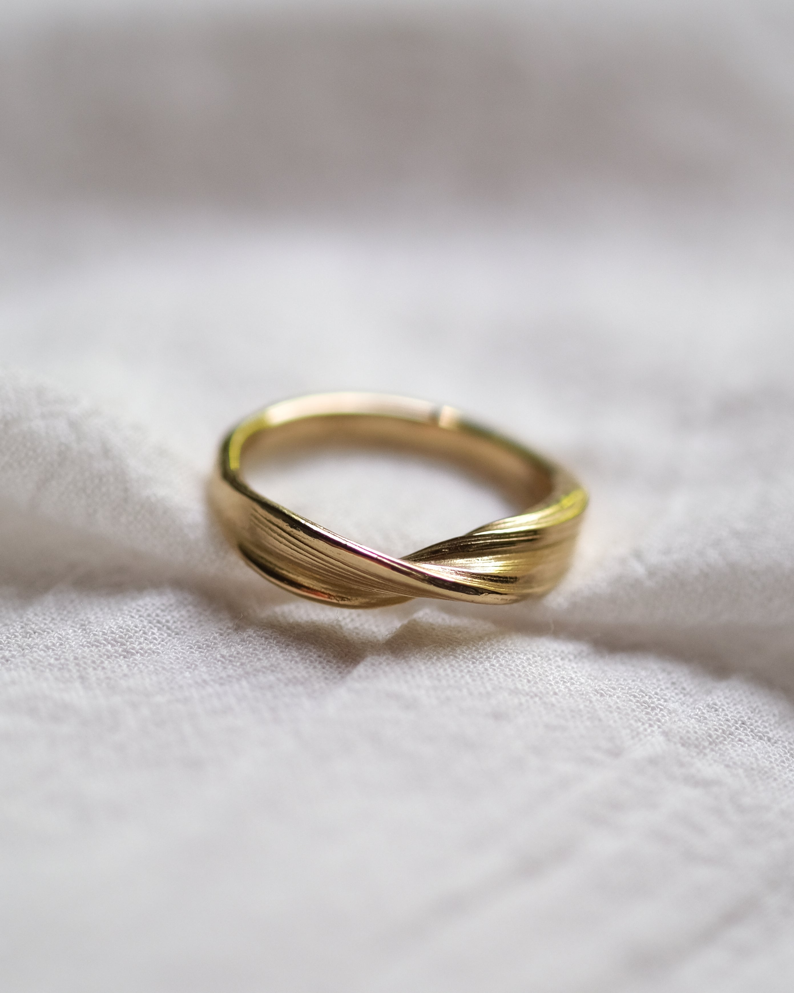 Gold ring with a twisted design on a white fabric background